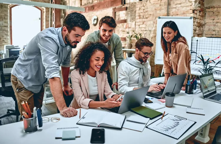 Group of male and female coworkers surrounding laptops at workspace